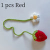 A handmade crochet red strawberry pendant with a white flower detail on a green thread.