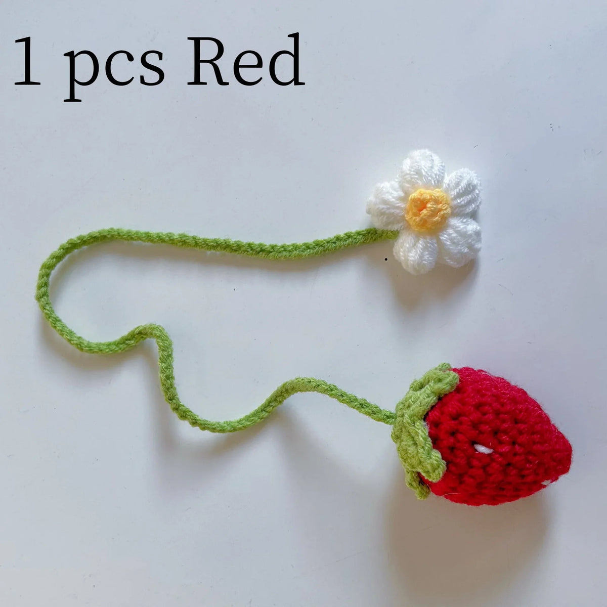 A handmade crochet red strawberry pendant with a white flower detail on a green thread.