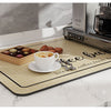 A light wood coffee mat is placed on a marble countertop next to a coffee maker and various coffee accessories.