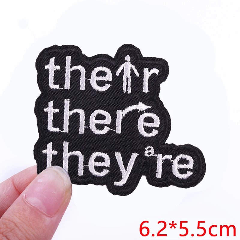 Black embroidered iron-on letter patches spelling out 'the there they are' on a finger