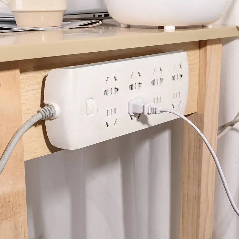 A white electrical outlet with multiple adhesive wall hooks is mounted on a wooden cabinet surface.