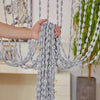 A hand is adjusting a gray bohemian tassel curtain with decorative lanterns for doorways.