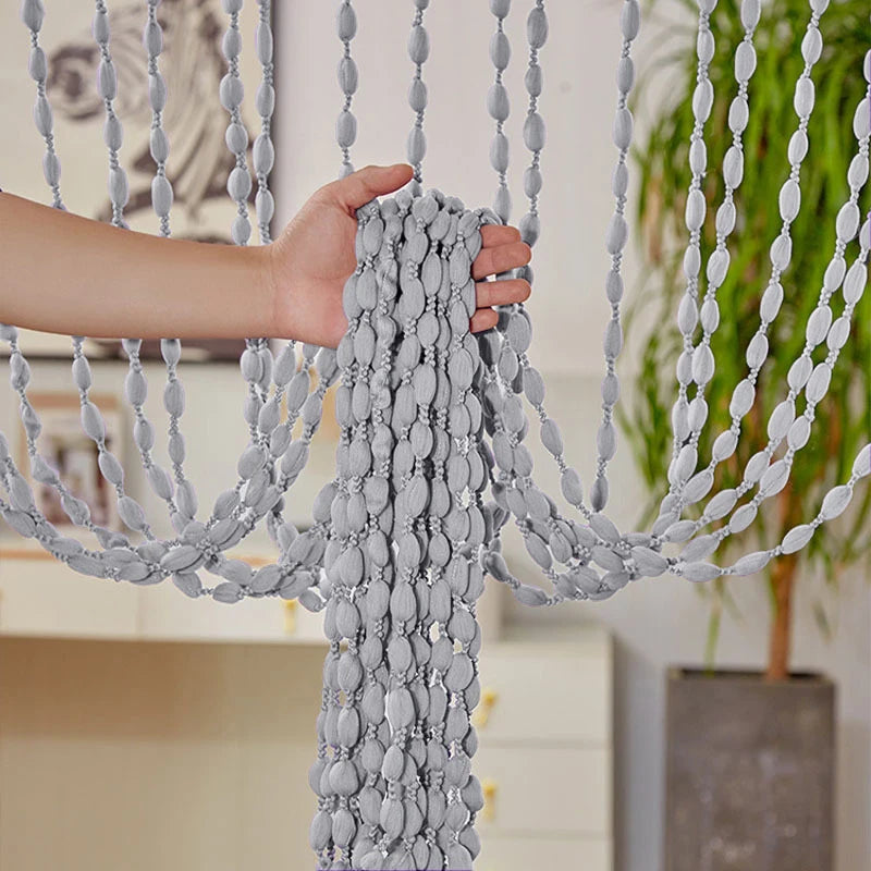 A hand is adjusting a gray bohemian tassel curtain with decorative lanterns for doorways.