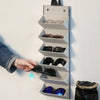 A hand is placing a pair of sunglasses into a vertical, multi-slot organizer case.
