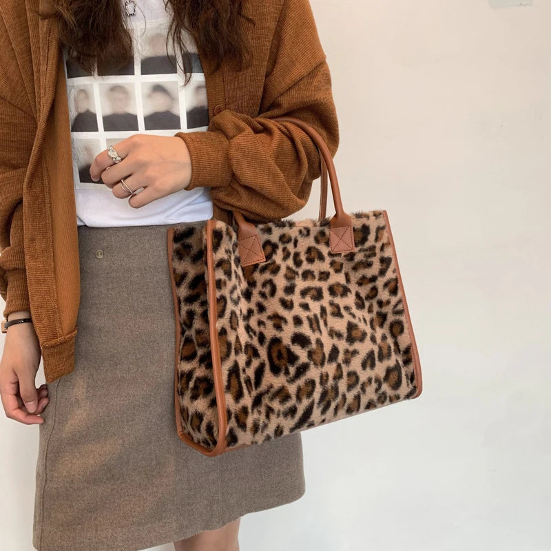 A woman holds a brown faux fur leopard print tote bag against a white shirt and a tan skirt.