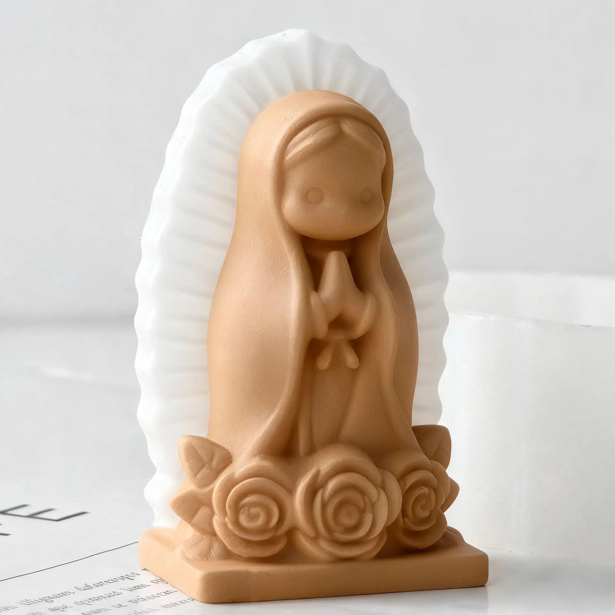 A terracotta silicone mold of a praying girl with hands clasped, set against a white background.