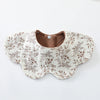 A beige cotton baby feeding bib with a brown floral pattern and a padded opening.