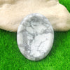 A smooth, oval white and gray marble stone rests on vibrant green grass.