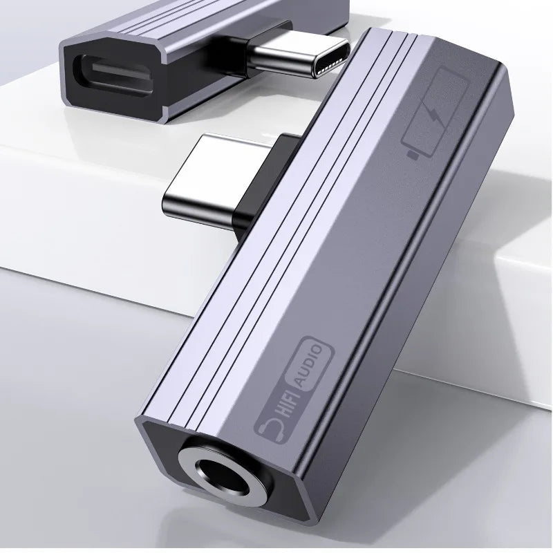 A silver USB-C to 3.5mm audio adapter with charging support is shown on a white surface.