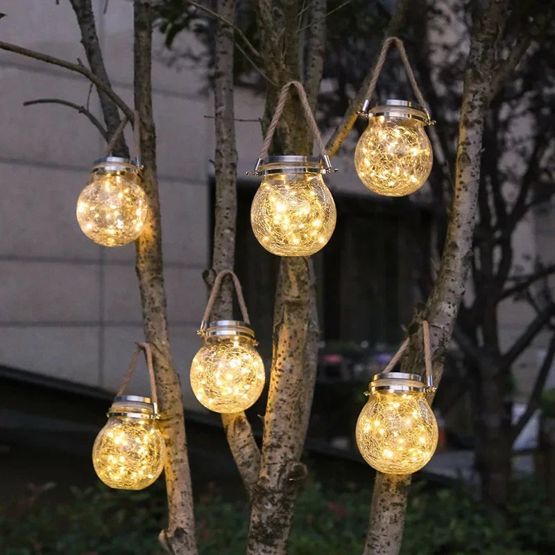 A cluster of warm glowing glass lanterns hanging from tree branches in an outdoor setting.