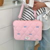 A pink quilted laptop shoulder bag with a light pink strap is being held by a person wearing a white shirt and jeans.