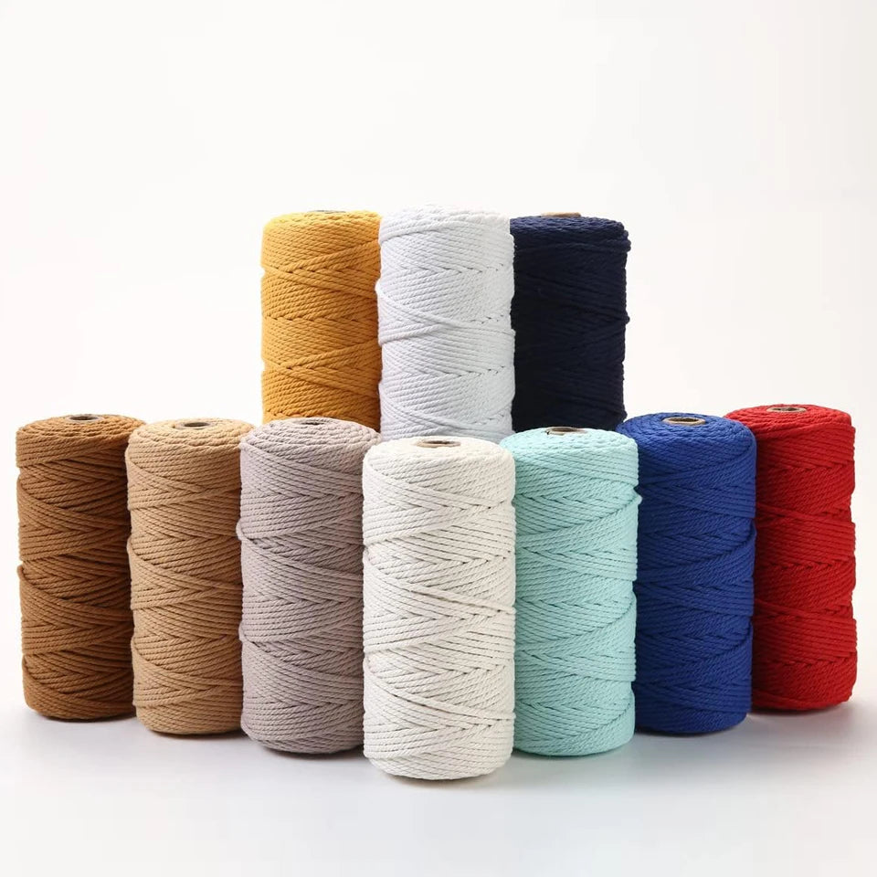 A collection of spools of 100% cotton macrame cord in various shades including beige, white, blue, and red.