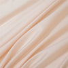 Close-up of a flowing, light peach or blush colored bamboo flat sheet fabric.