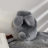 A gray plush rabbit hot water bottle with a soft flannel cover resting on a textured gray fabric.