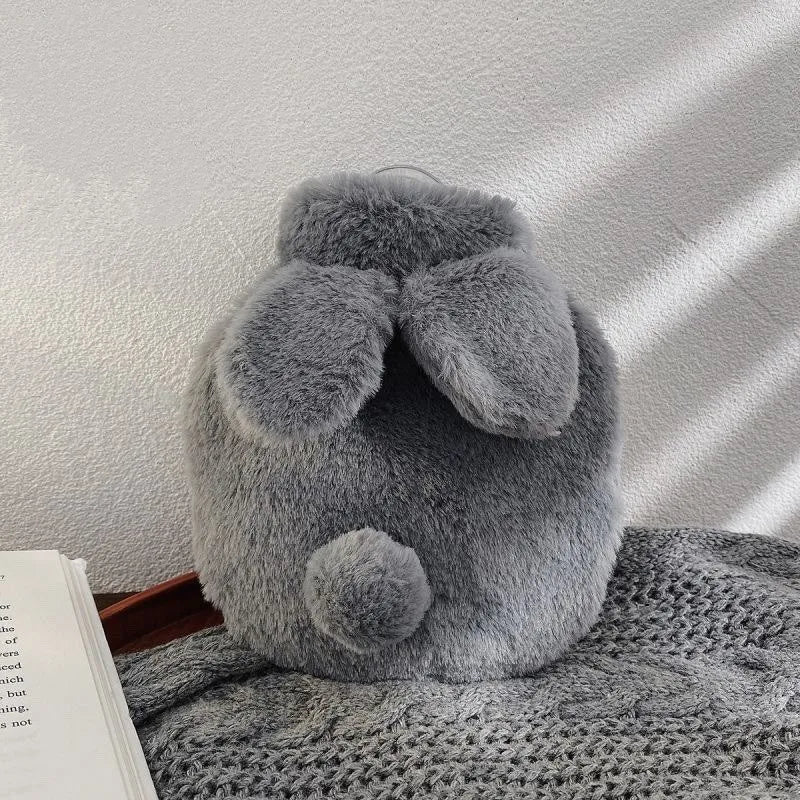 A gray plush rabbit hot water bottle with a soft flannel cover resting on a textured gray fabric.