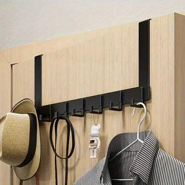 A black over-the-door coat rack with six hooks mounted on a light wood panel.