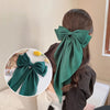 A dark green silk bow hair clip tied around a ponytail holder.