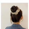 A woman's dark hair is styled in a bun with a light beige plush coil hair tie visible on top.