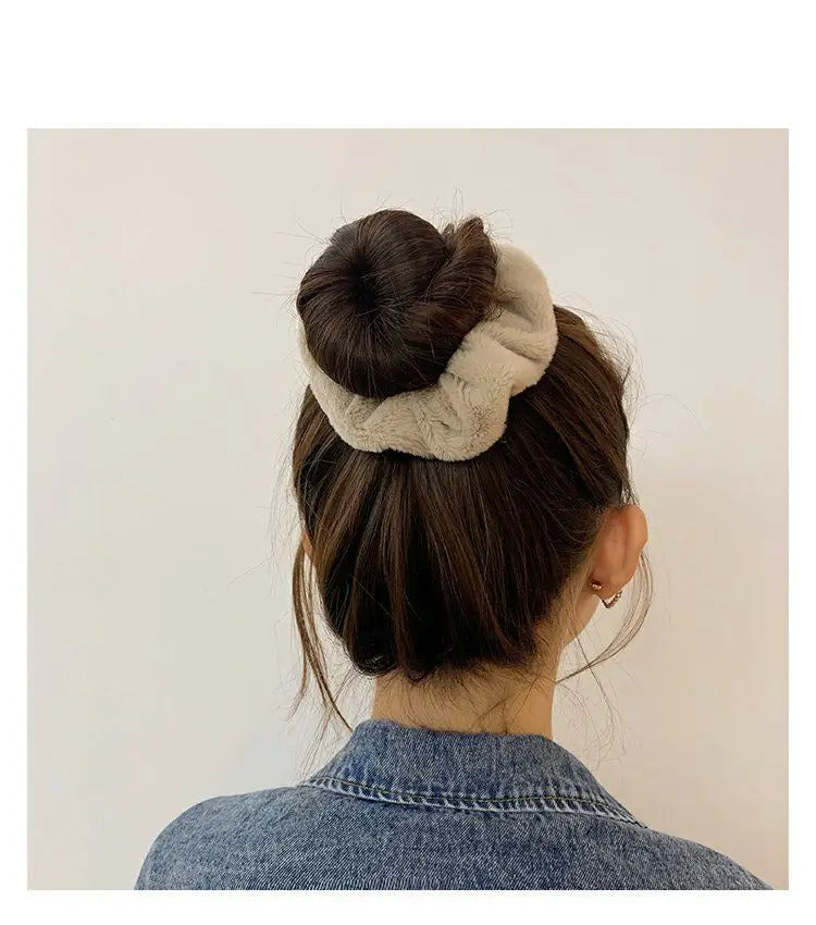 A woman's dark hair is styled in a bun with a light beige plush coil hair tie visible on top.