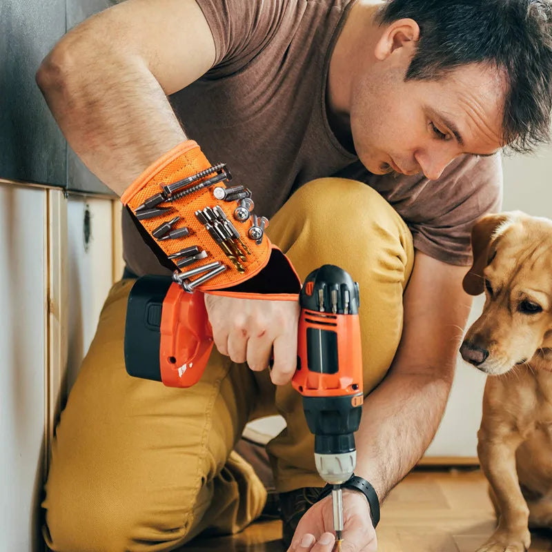 A man is using an orange magnetic wrist strap tool to hold small tools while working on something.