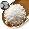 White natural soy wax granules in a gold-colored dish with small white wax pieces.