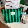 A black and green striped canvas cosmetic bag is displayed on a counter next to a menu.