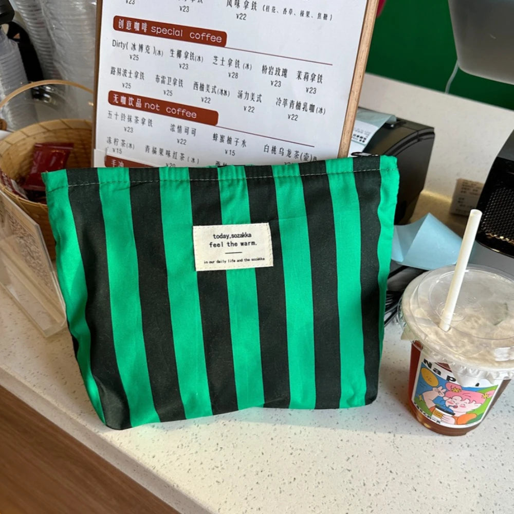 A black and green striped canvas cosmetic bag is displayed on a counter next to a menu.