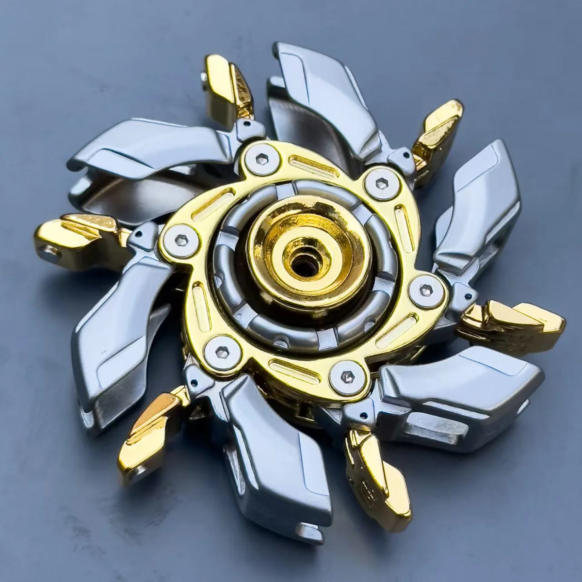 A precision metal fidget spinner with silver and gold components is shown against a gray background.
