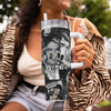 A person holds an insulated stainless steel tumbler with a straw lid featuring a graphic design.