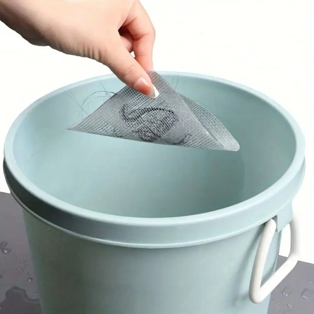 A hand places a disposable drain hair catcher sticker into a light blue plastic bucket.
