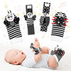 A set of black and white baby wrist and foot rattles sensory toys shown above a sleeping baby.