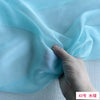 A hand is gently folding a piece of light blue sheer chiffon fabric.