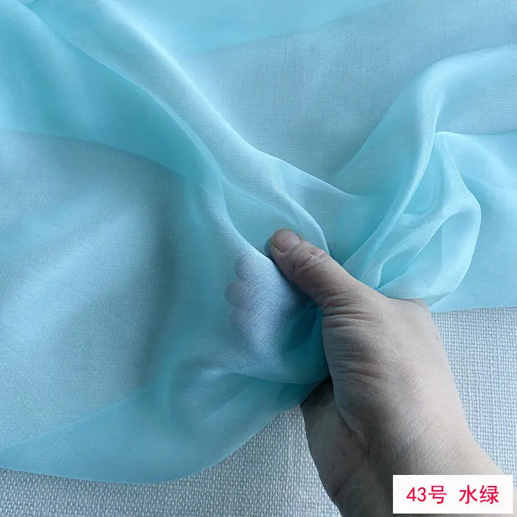 A hand is gently folding a piece of light blue sheer chiffon fabric.
