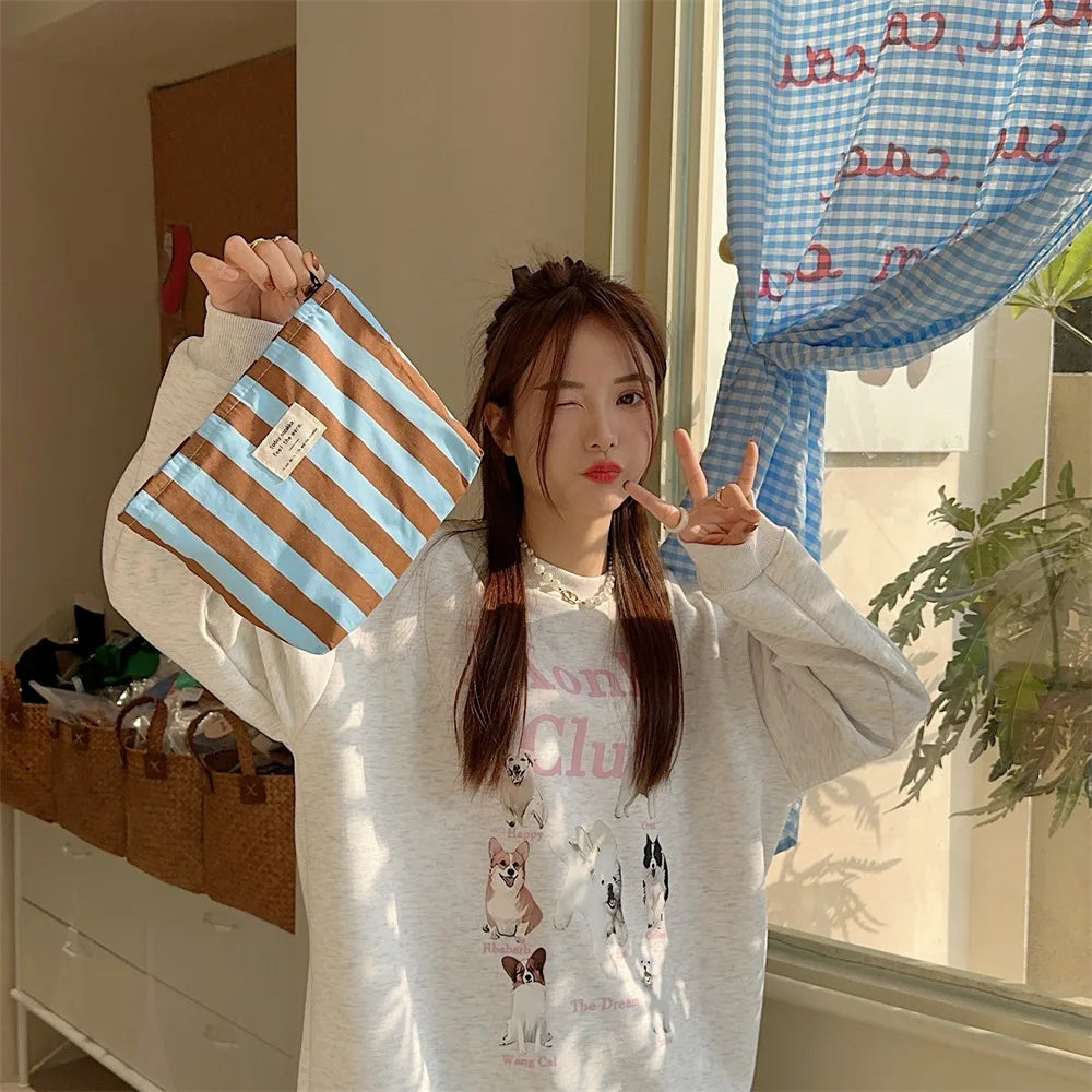 A person holds a striped canvas cosmetic bag in a selfie pose indoors.