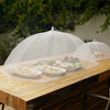 A collapsible mesh food cover is placed over a wooden table containing various dishes for outdoor dining.