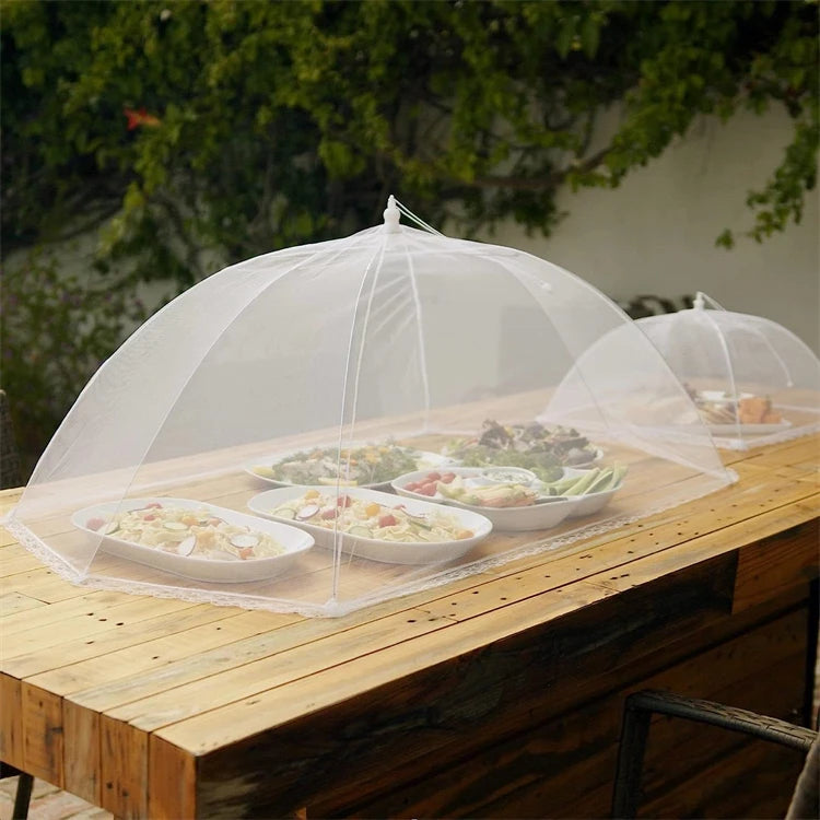 A collapsible mesh food cover is placed over a wooden table containing various dishes for outdoor dining.