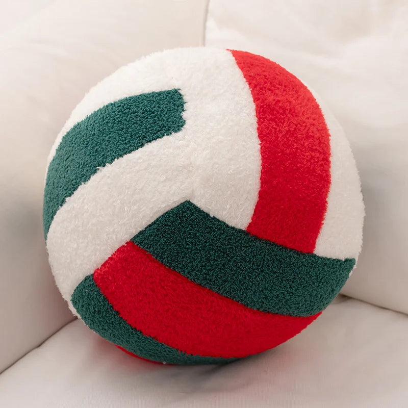 A round plush volleyball toy with stripes of white, red, and green fabric resting on a white surface.