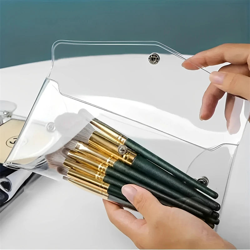 A hand holds a transparent cosmetic bag with a clear lid, inside which several gold and black makeup brushes are stored.