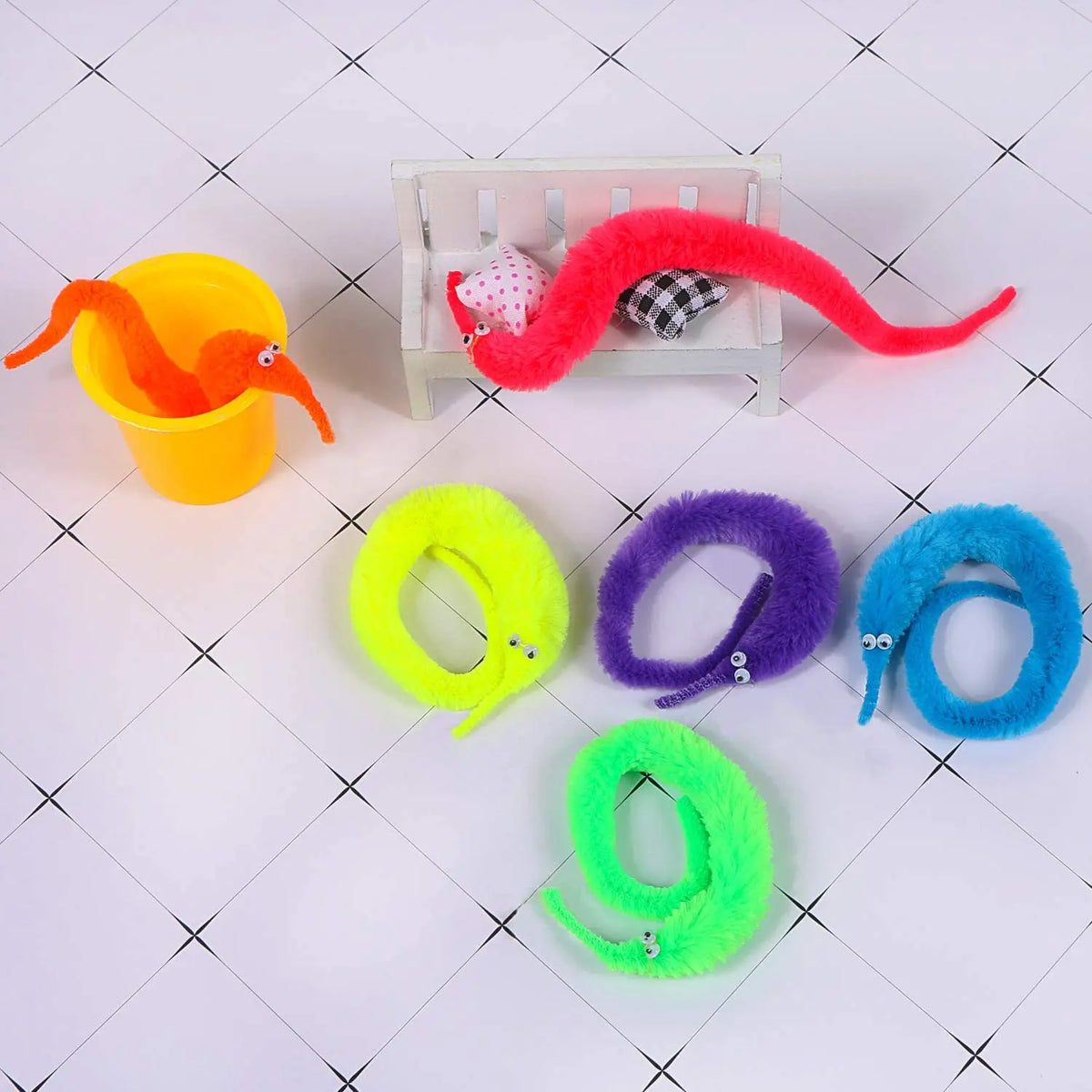 A collection of fuzzy wiggly worm magic trick items including an orange bowl, a red wiggly worm, and various colored elastic 