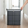 A hand is lifting a gray fabric storage organizer bag with black trim and silver buckles in a bright hallway.