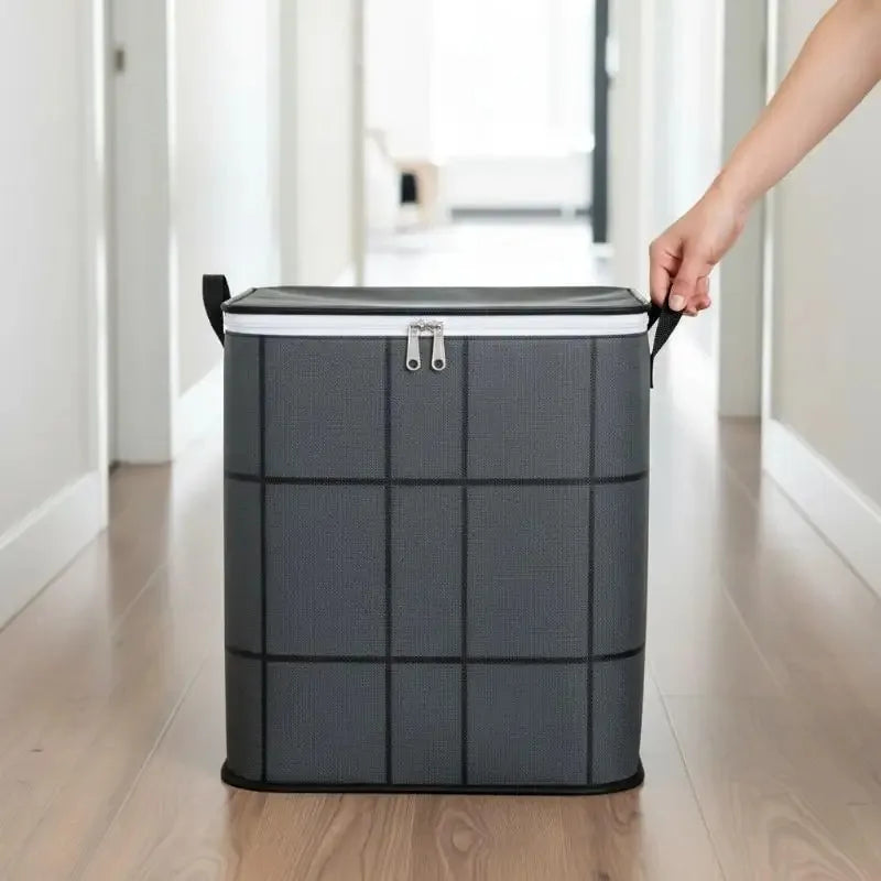 A hand is lifting a gray fabric storage organizer bag with black trim and silver buckles in a bright hallway.