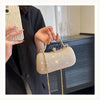 A hand holds a beige shimmering envelope clutch with a gold chain strap against a dark background.