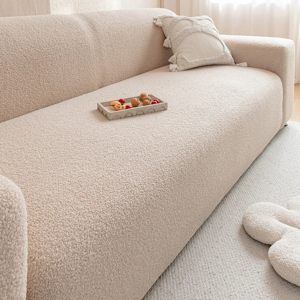 A light beige plush sofa with a matching throw pillow and a small tray of fruit on the seat.