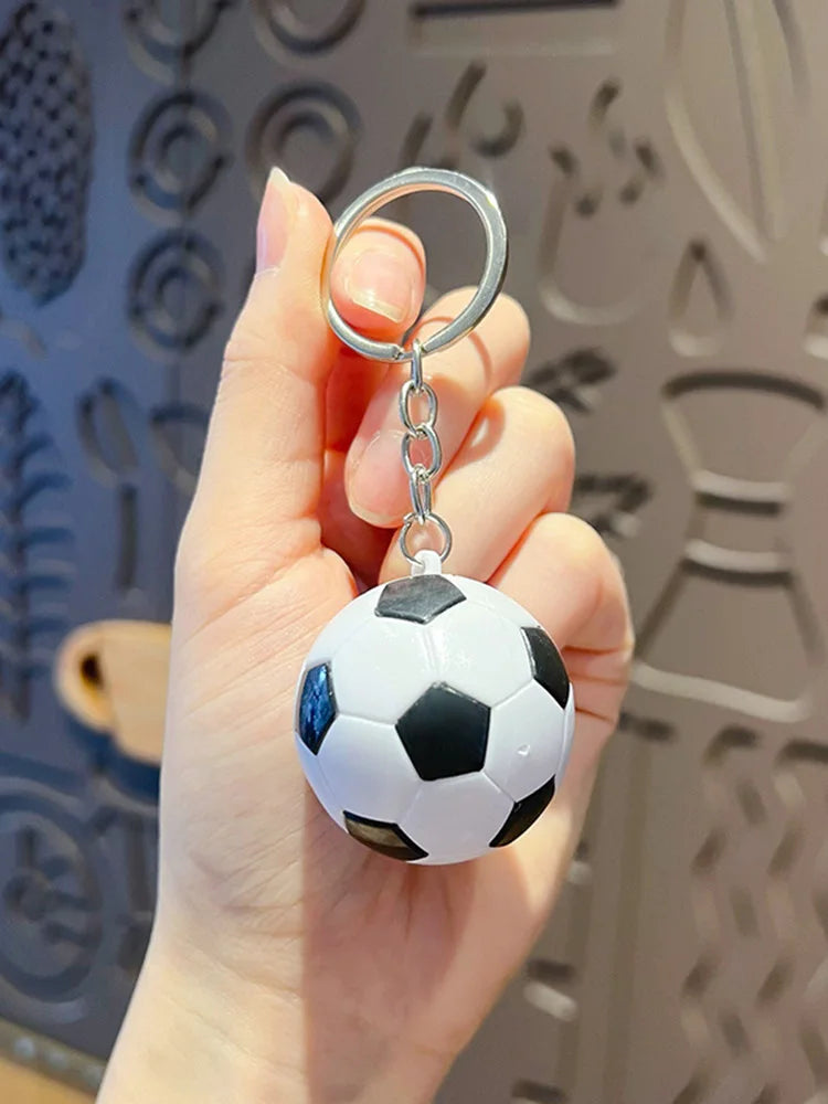 Una mano sostiene un llavero de pelota de fútbol metálica con patrón blanco y negro.