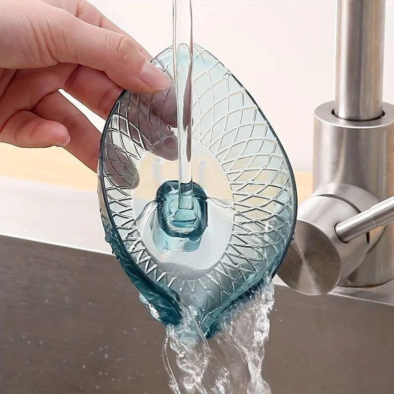 A hand holds a leaf-shaped glass soap dish with a suction cup, dripping water into a sink.