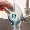 A hand holds a leaf-shaped glass soap dish with a suction cup, dripping water into a sink.