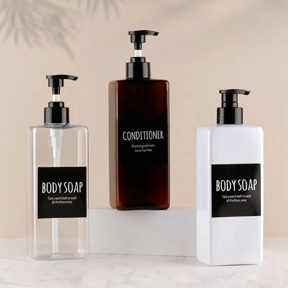 Three refillable soap dispenser bottles in glass and white with black labels for body soap and conditioner