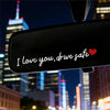 A car mirror features a decal with the text I love you drive safe and a red heart on a night cityscape background.