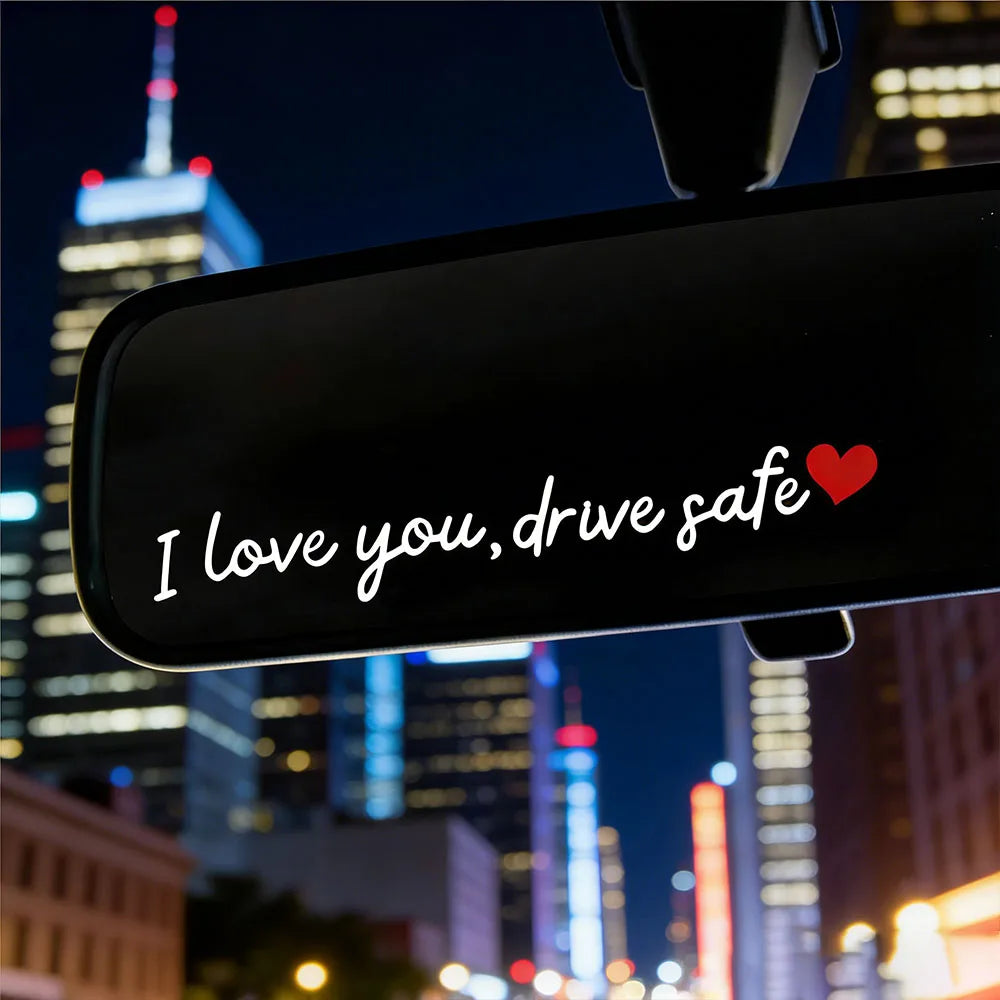 A car mirror features a decal with the text I love you drive safe and a red heart on a night cityscape background.