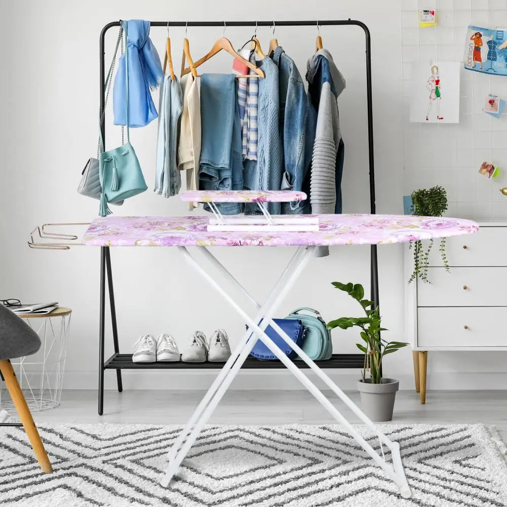 A purple ironing board with a pink top, holding various blue and gray clothing items on a black rack.